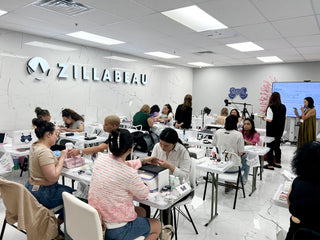 White seminar classroom for nail technicians as they practice art on each other. A company sign says, "Zillabeau" overhead.